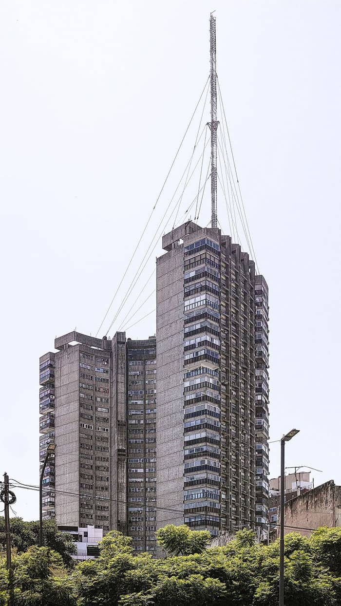 A grim, weathered concrete high-rise apartment tower topped with a massive radio antenna tower
