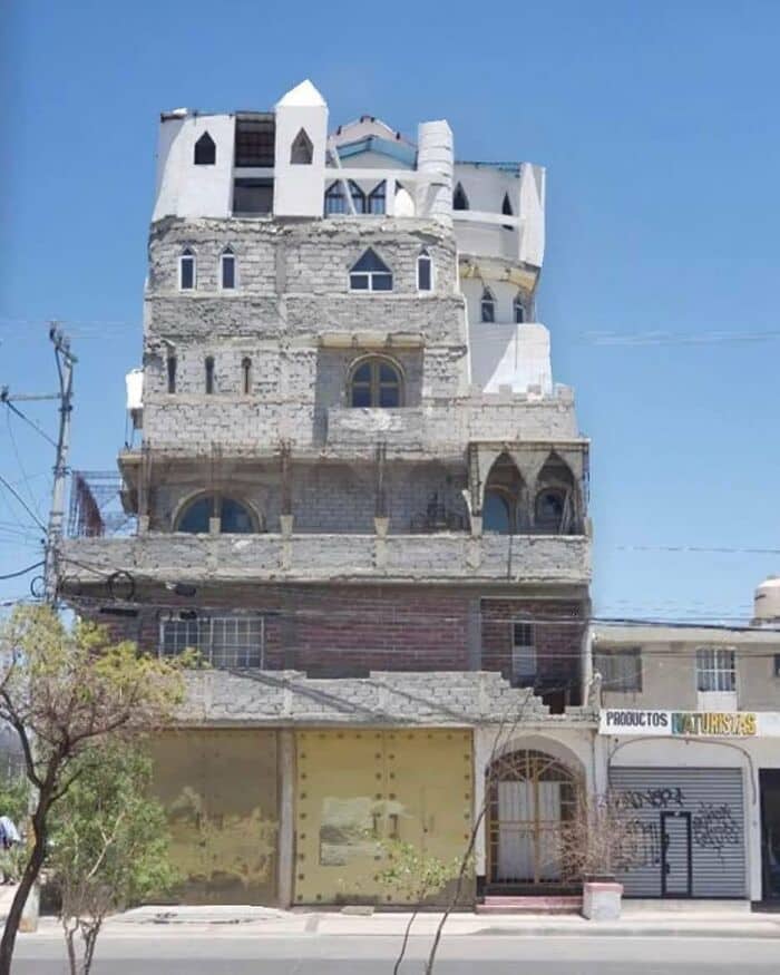 An unfinished, mismatched multi-story concrete building with chaotic architectural styles and pointed turrets.