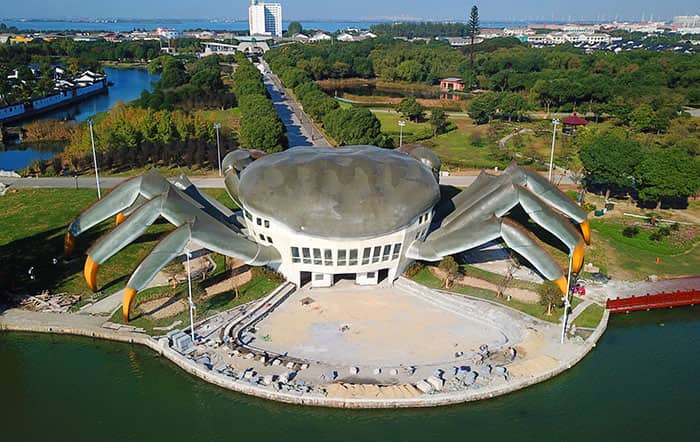 An aerial view of a large building shaped like a giant crab sitting by the water.