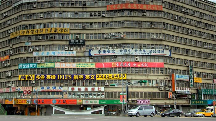 A massive, dingy concrete commercial complex covered in a chaotic mess of colorful business signs.