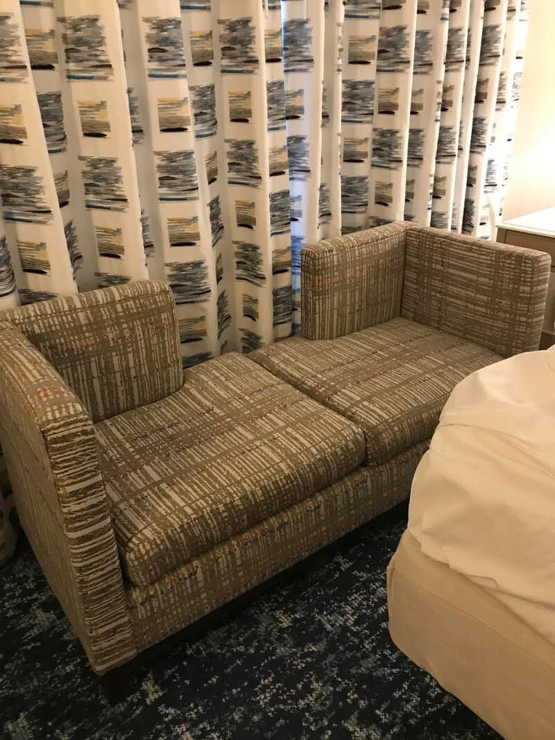 Patterned green and tan sofa with high armrests positioned in front of matching curtains.