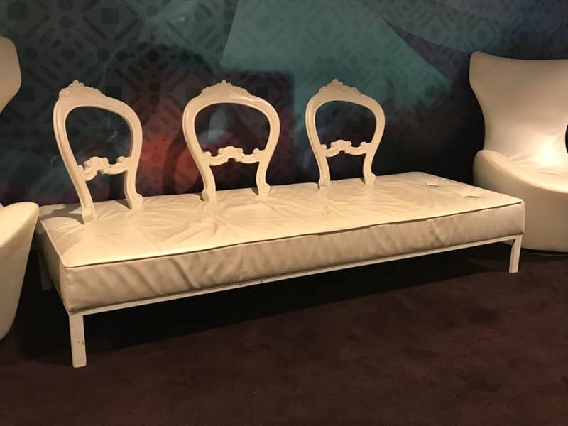 Long white leather bench sofa with three ornate wooden chair backs attached.