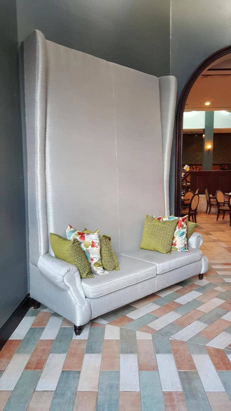 Light gray sofa with an impossibly tall, 10-foot-high backrest against a dark wall.