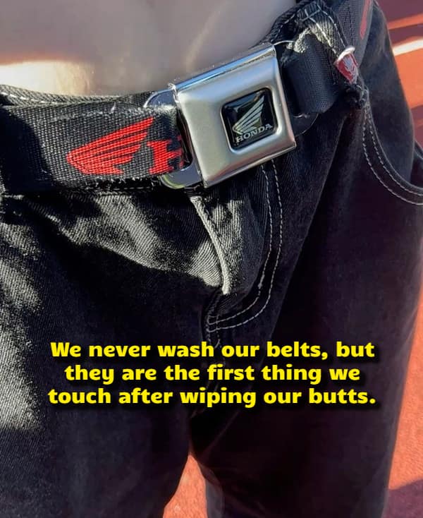 A tight close-up of a person's waist wearing black denim jeans with a custom belt made from a vintage Honda seatbelt buckle frames a disturbingly accurate visual funny shower thought regarding unwashed wardrobe accessories.