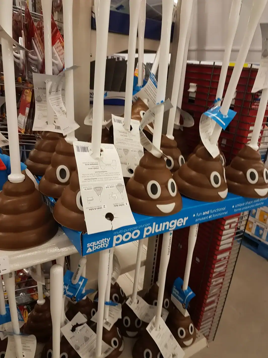 A retail shelf stocked with "Poo Plungers," featuring a weird product design where the rubber plunger head is shaped exactly like the smiling brown poop emoji.
