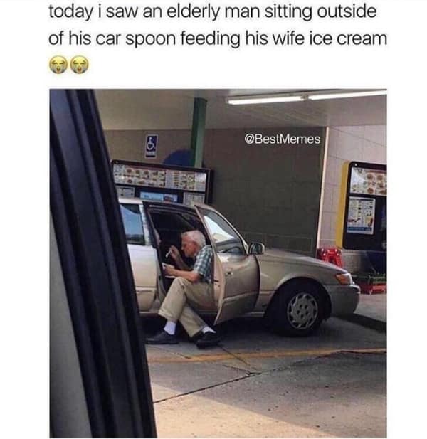 A candid, high-octane wholesome meme showing an elderly man sitting on the edge of his car seat at a drive-in, tenderly spoon-feeding ice cream to his wife who is sitting inside the vehicle.