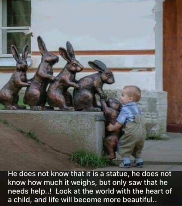A heart-melting wholesome meme of a toddler in overalls reaching down to grab the paw of a bronze bunny statue to help it climb a stone ledge where three other rabbit statues are already waiting.