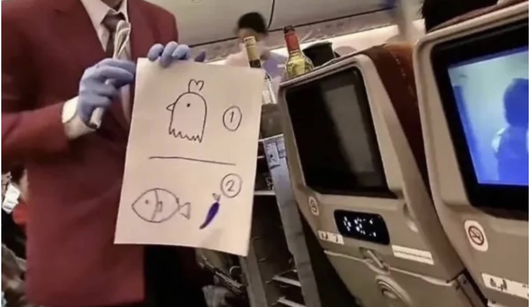 Flight attendant on an airplane holding up a hand-drawn sign of chicken, fish, and eggplant options.