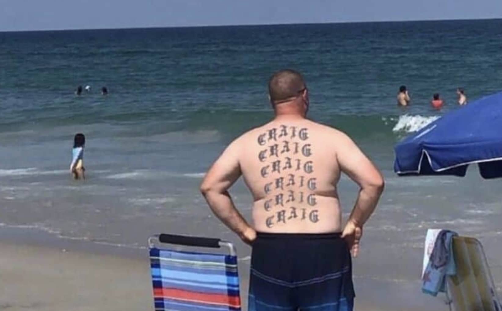 Man standing on a beach with the name Craig tattooed multiple times across his back.
