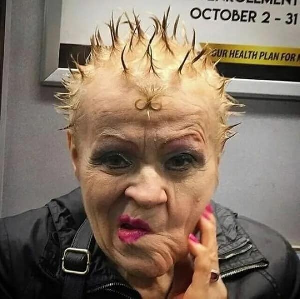 Close-up portrait of an older woman showcasing a haircut fail with short blonde liberty spikes and a small gelled infinity loop on her forehead.