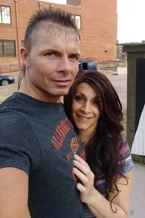 Man standing with a woman showing a unique haircut fail featuring a spiked top, a mullet back, and thin comb-over micro bangs on his forehead.