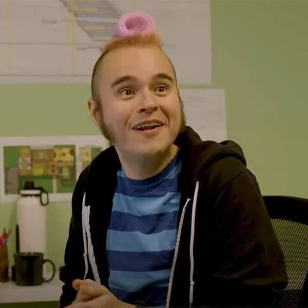 Man in a blue striped shirt smiling with a tiny mohawk topknot wrapped in a bright pink hair roller, showcasing unusual bad haircuts.