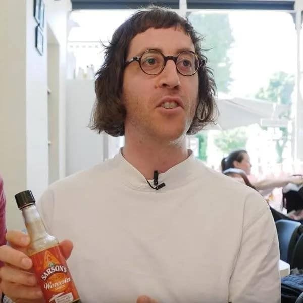 Man with round glasses holding a bottle of Worcester sauce with an uneven pageboy bob and choppy bangs, an example of bad haircuts.