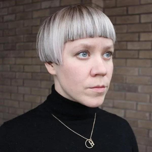 Woman with a silver-grey geometric bowl cut and sharp blunt bangs looking sideways, framed as a severe haircut fail.