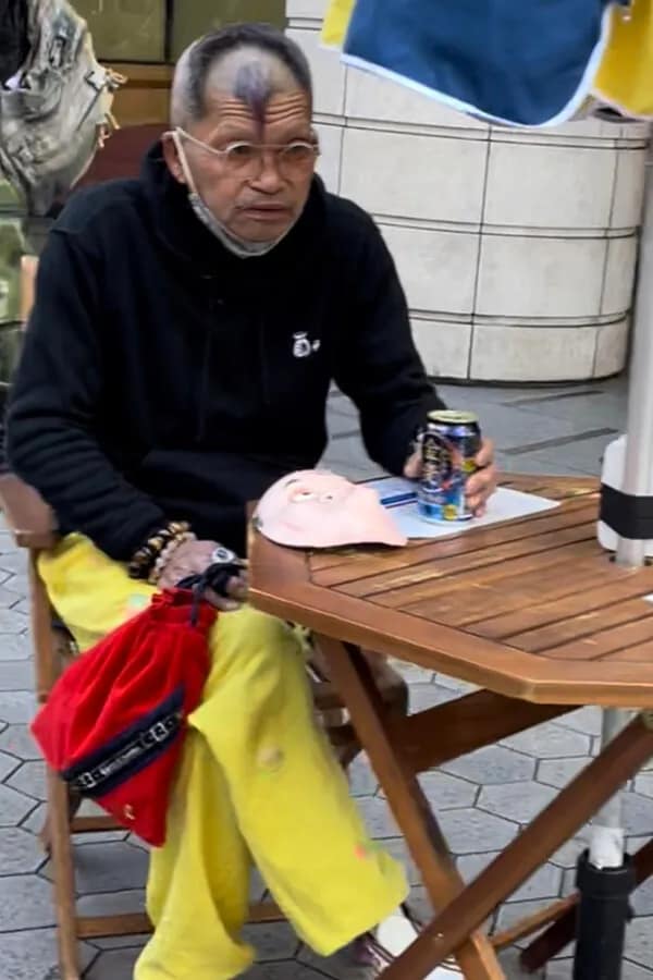 Older man at a table with a shaved head featuring a lone, dark strip of hair left on the center of his forehead, illustrating unique bad haircuts.