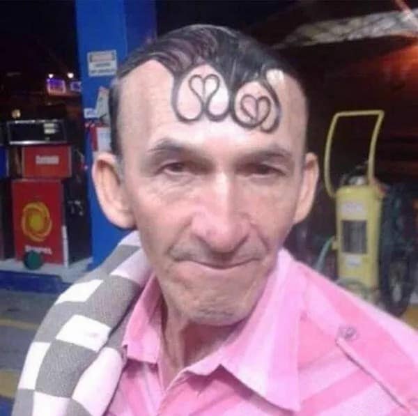 Close-up of a man with front fringe hair styled into gelled heart shapes on his forehead, a romantic haircut fail.
