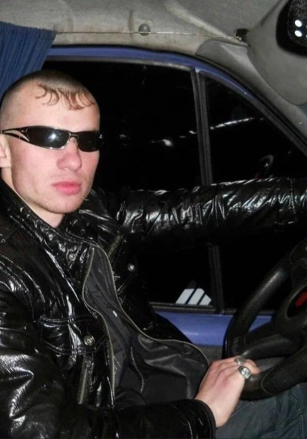 Man in a car with a shaved head featuring a tiny patch of curled front fringe bangs, a hilarious haircut fail.