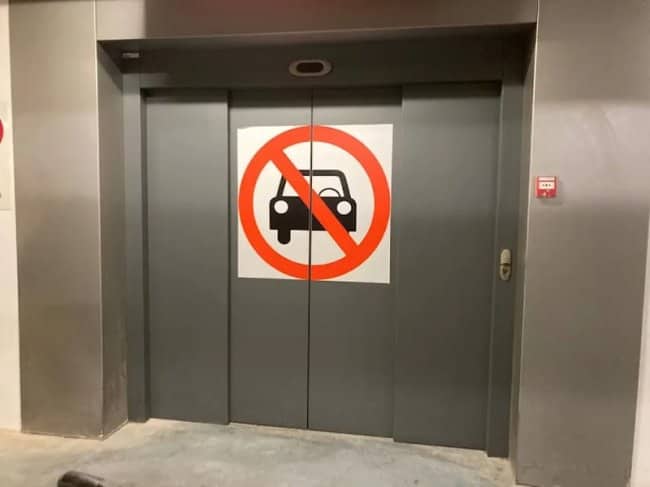 Amusing elevator door sign with a graphic explicitly banning cars inside the elevator.