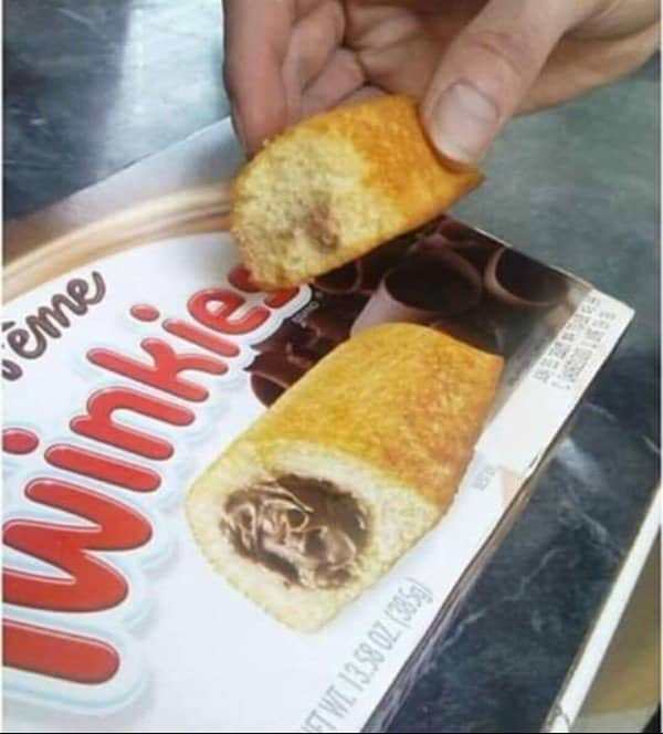 Blursed image of a hand holding a chocolate Twinkie next to the product packaging.