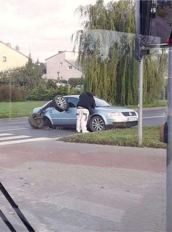 A catastrophic mechanical suspension breakdown showing an elite car fail where the rear axle of a light blue Volkswagen sedan has completely sheared off, leaving the entire wheel assembly flipped upside down against the rear glass.