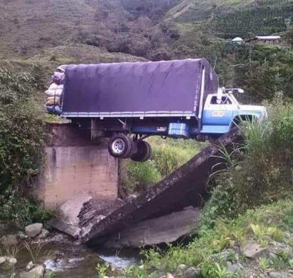 A dramatic structural collapse and car fail tracking a blue cargo truck perfectly suspended mid-air across a deep canyon gap after the concrete bridge slab entirely dissolved beneath its wheelbase.