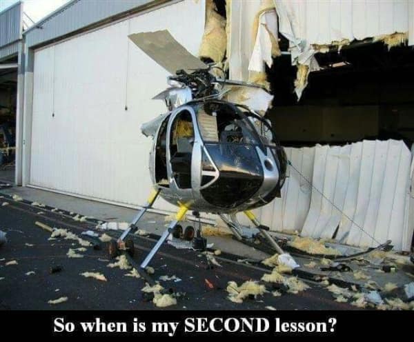 An unhinged aviation car fail macro displays a small silver helicopter that has crashed tail-first directly into the side of a corrugated metal hangar wall, paired with the sarcastic caption, "So when is my SECOND lesson?"