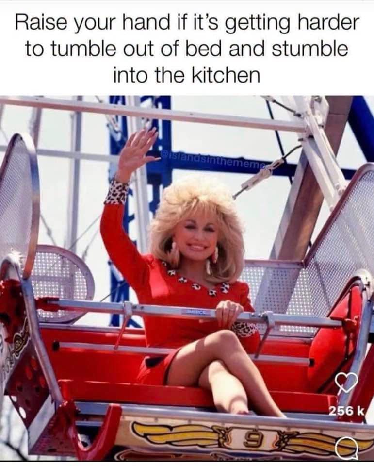 An absolute gem of classic memes nostalgia features country music icon Dolly Parton lounging gorgeously inside a red amusement park Ferris wheel cart. Smiling radiantly with her signature voluminous blonde hair, she raises her hand to the camera to perfectly match the relatable text overhead: "Raise your hand if it's getting harder to tumble out of bed and stumble into the kitchen."