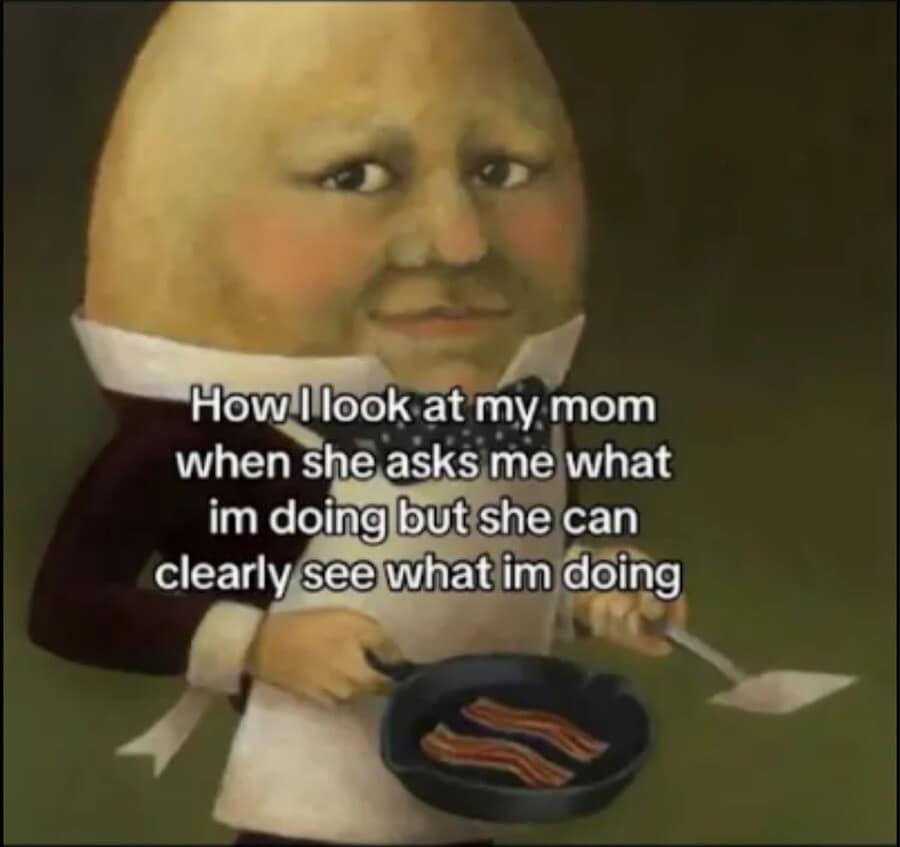 A deadpan domestic old meme captures a realistic, historical-style painting of a smug Humpty Dumpty wearing a suit and apron while frying strips of bacon, captioned with the text: "How I look at my mom when she asks me what im doing but she can clearly see what im doing."