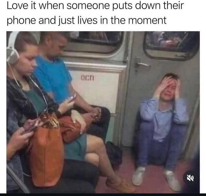 humorous social commentary classic meme presents a photo of a crowded subway car under the text: "Love it when someone puts down their phone and just lives in the moment". While the surrounding commuters are completely buried in their smartphones, one man in a light blue shirt is sitting directly on the train floor in a state of absolute emotional distress, holding his face in his hands.