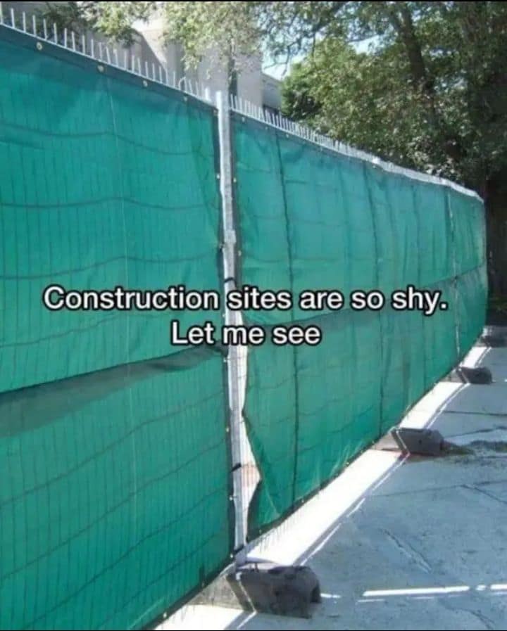 A perspective street shot of a tall green safety mesh fence screening off a municipal walkway in a playful classic meme overlaid with white text: "Construction sites are so shy. Let me see".
