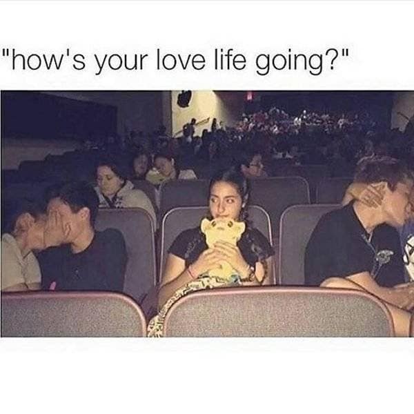 A classic meme image macro answering the question "how's your love life going?" with a photograph of a woman sitting completely alone in a crowded movie theater row cradling a stuffed Simba plush toy, flanked on both sides by couples intensely making out.
