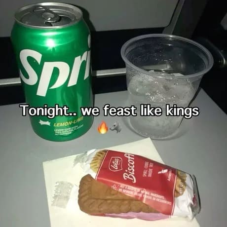 A classic memes economic travel picture capturing an airplane economy tray table holding a single green can of Sprite, a plastic cup of ice, and one wrapped pack of Lotus Biscoff cookies, dramatically captioned: "Tonight.. we feast like kings".