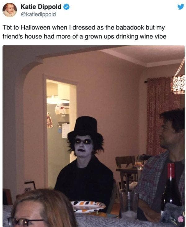 A viral holiday snapshot shared across platforms as a classic meme highlights a tweet by Katie Dippold showing a person in a terrifying, pitch-black Babadook costume sitting awkwardly at a casual adult wine night.