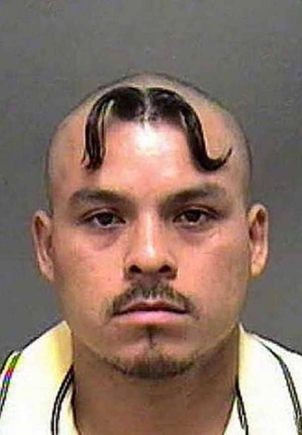 Mugshot of a bald man with a thin mustache styled on top of his forehead.