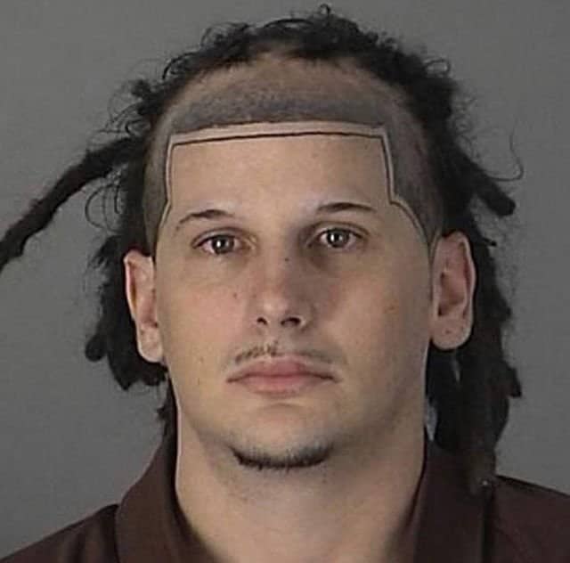 Mugshot of a man with dreadlocks and a perfectly rectangular shaved forehead line.