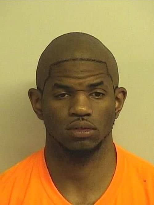 Mugshot of a bald man with a thin tattooed or drawn hairline across his scalp.