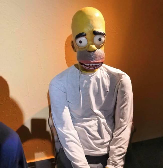 Distortive, hyper-uncanny human sized wax figure version of Homer Simpson in a white shirt.
