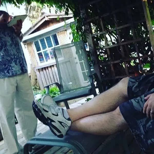 A dad reclining on a patio chair wearing white chunky sneakers and camo cargo shorts next to a trellis.