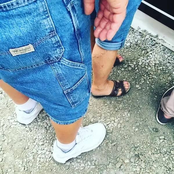Top-down view of a dad wearing light wash Wrangler denim shorts and crisp white sneakers on gravel.