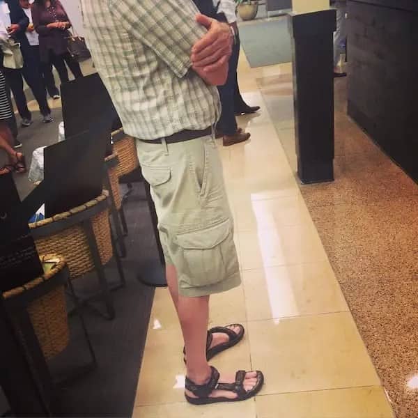 A dad standing in line wearing a plaid button-up shirt, tan cargo shorts, and strappy black sport sandals.