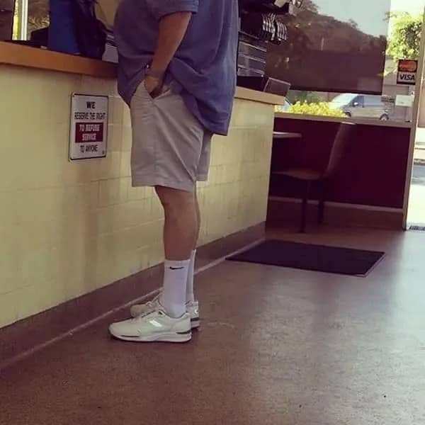 Side profile of a dad waiting inside a fast food restaurant wearing an oversized purple shirt and light khaki shorts.