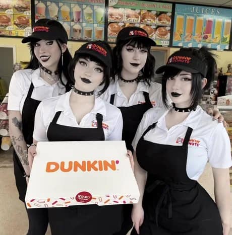 A stylized alt-culture donut meme featuring four workers wearing gothic and e-girl fashion—complete with dark makeup, black lipstick, and spiked chokers—while sporting Dunkin' uniform aprons and visors as they hold up a classic white donut box.