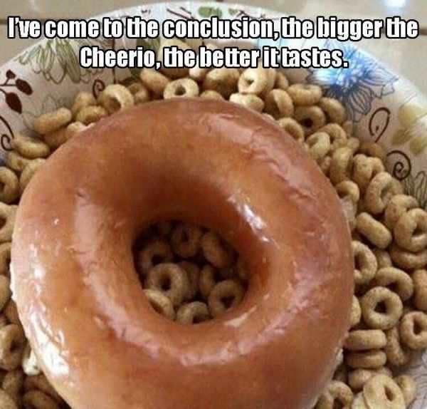 A breakfast-themed donut meme showing a large, glistening glazed donut sitting directly in the center of a bowl filled with Cheerios cereal, complete with top text declaring that the bigger the Cheerio, the better it tastes.