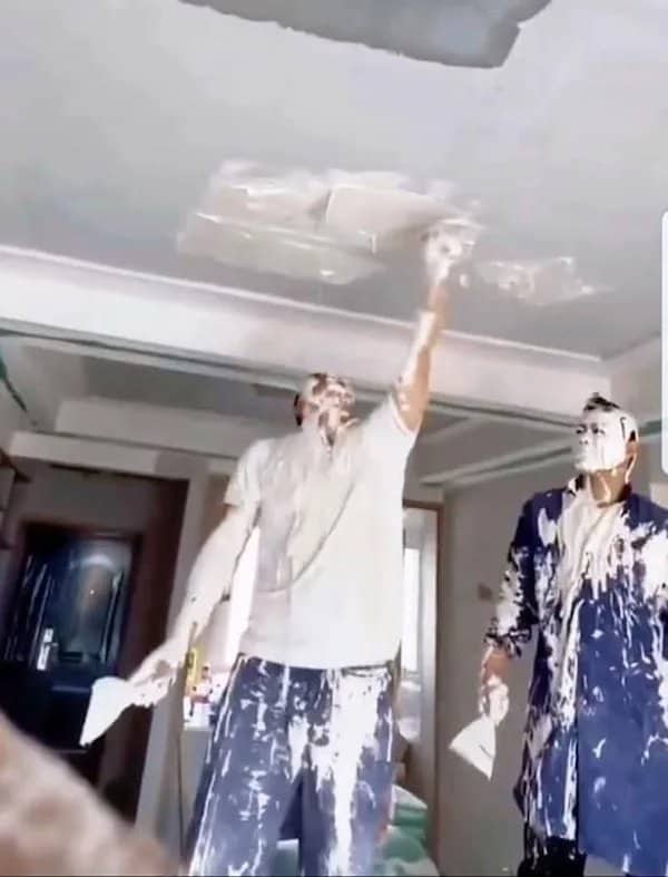 Two construction workers completely covered in wet white ceiling plaster inside a room.