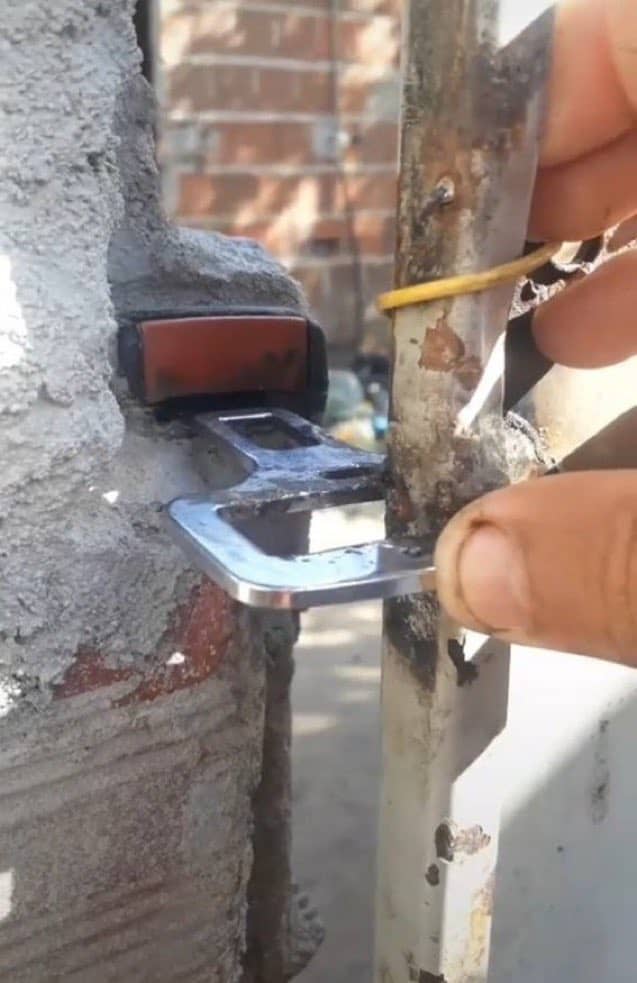 Redneck engineering fail with a car seatbelt buckle welded to a rusted outdoor gate.