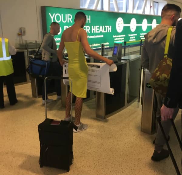 A man wearing a tight yellow dress and fishnets scans his ticket at airport security.