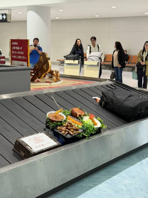 A giant, realistic display of assorted Japanese food dishes circulating on an airport baggage carousel.