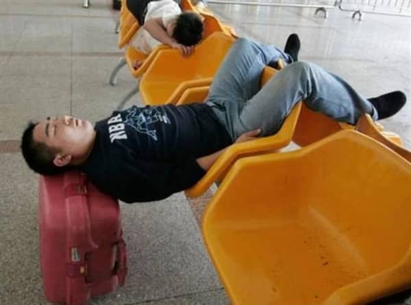 A man sleeps across uncomfortable plastic airport terminal chairs by bridging his body between them.