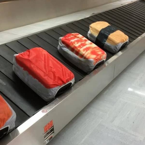 Three suitcases covered in fabric protectors that look exactly like giant pieces of nigiri sushi.