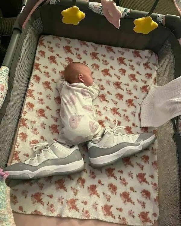 A sleeping baby in a crib wearing massive gray and white basketball sneakers.